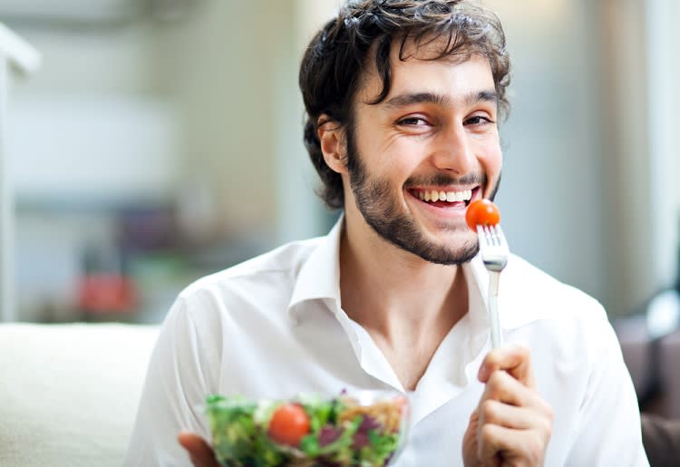 Smiling man holding a tomato on a fork to his mouth