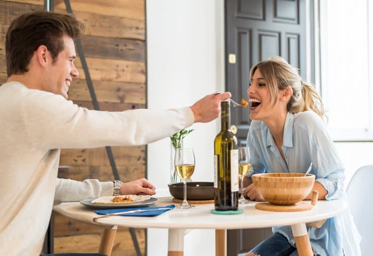 Man feeding his partner a bite of his food at a table